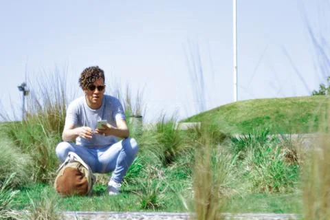 Man using mobile and squatting outdoors with a sports bag Stock Photos