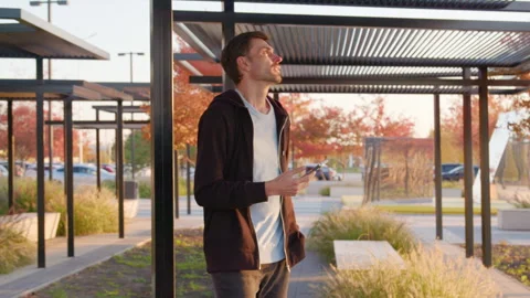Man using mobile app to unlock rental car in urban park setting, surrounded by Stock Footage 315530065