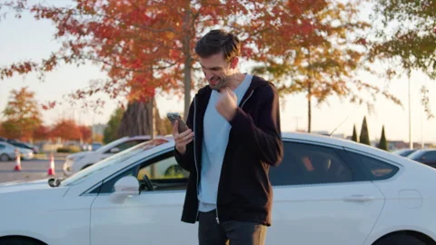 Man using mobile application to unlock rental car in urban setting, surrounded Stock Footage 315530270