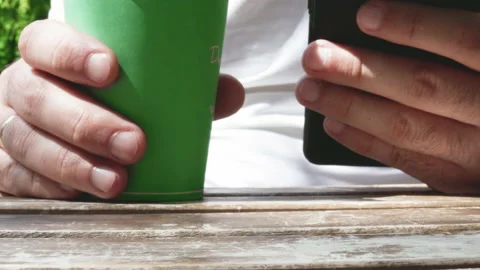 Man using mobile phone and drink coffee in public park,wooden table Vidéo 196822178