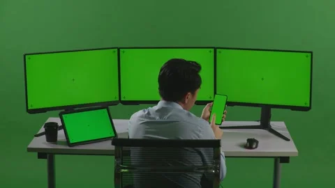 Man Using Mobile Phone And Multiple Computer Monitor With Mock Up Green Screen Stock Footage 249625123