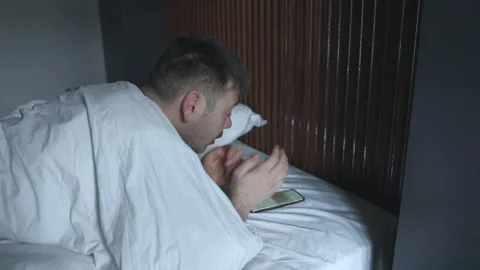 Man using mobile phone, browsing internet and texting on phone lying in bed Stock Footage 171981010