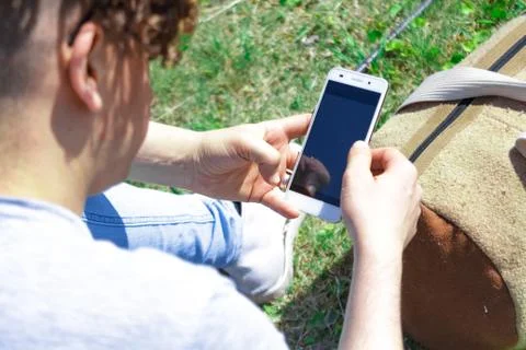 Man using a mobile phone sitting on the grass with a sports bag Stock Photos
