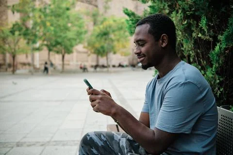 Man using a mobile phone sitting on a bench outdoors. Stock Photos