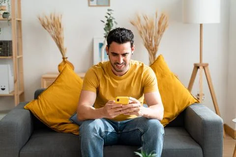Man using mobile phone sitting on living room sofa. Stock Photos
