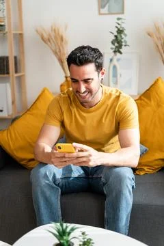 Man using mobile phone sitting on living room sofa. Stock Photos