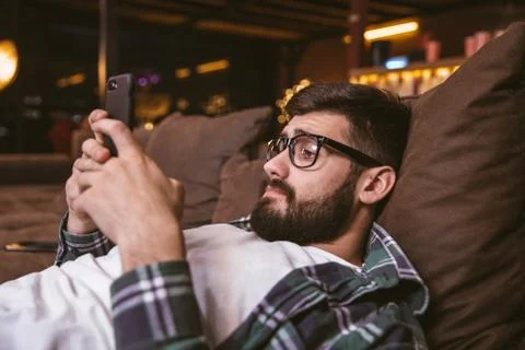 Man using mobile phone while lying on sofa at home. Lifestyle concept Stock Photos