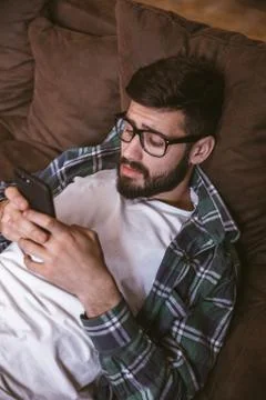 Man using mobile phone while lying on sofa at home. Lifestyle concept Stock Photos