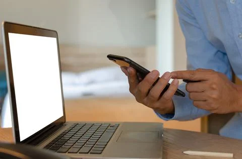 Man using mobile smart phone and computer laptop on desk Stock Photos