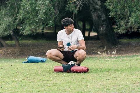 Man using a mobile squatting next to a yoga mat outdoor Stock Photos