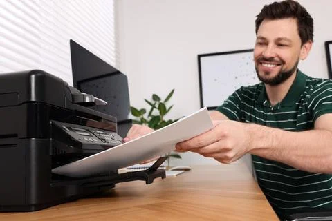 Man using modern printer at wooden table indoors, selective focus Foto stock