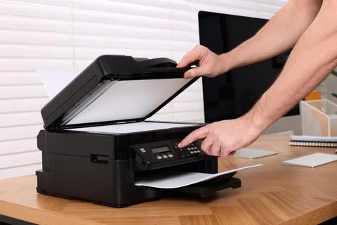 Man using modern printer at wooden table indoors, closeup Stock Photos