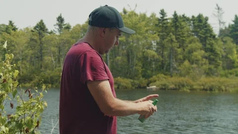 Man Using Mosquito Repellent Spray by the Lake in Sunshine Stock Footage 280394389
