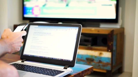 Man using multiple devices at same time; phone, laptop and TV screens, Video stock 121716671