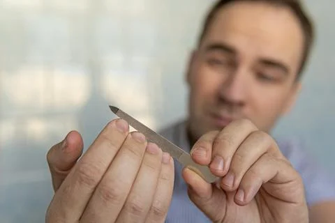 Man using a nail file. man cuts his own nails with scissors on a blue backg.. Stock Photos