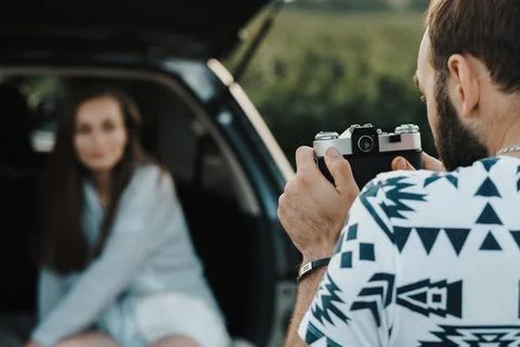 Man using old film camera to photography his girlfriend who sitting inside trunk Stock Photos