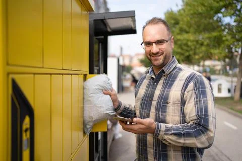 Man using a package delivery locker on a sunny day in an urban setting while Stock Photos