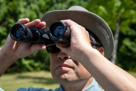 A  man using a pair of binoculars to look at something in the sky. Stock Photos