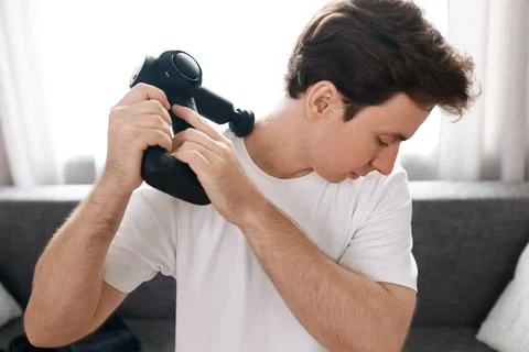 Man using a percussion massage gun on his neck and shoulder for pain relief.. 库存照片