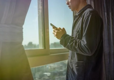 Man using phone and standing by the window Stock Photos