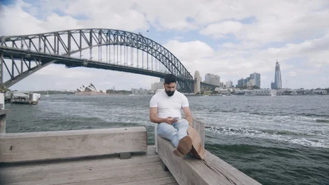 Man Using Phone on Bench by Sydney Harbour Bridge. Wide Shot Dolly Stockbeeldmateriaal 129363582