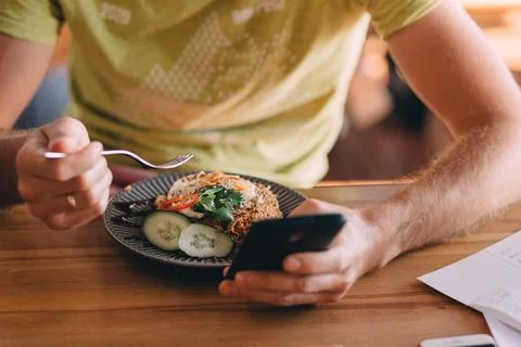 Man using phone during lunch in a cafe, man eating fried rice, concept of using Stock Photos