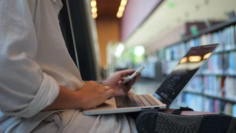 Man Using Phone With Laptop In Library, Representing Digital Study Vídeo Stock 334436975