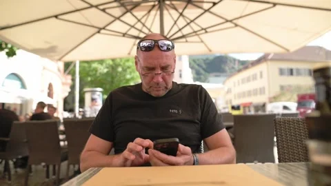Man using phone at outdoor cafe under umbrella in Italian street Vídeo Stock 318195376