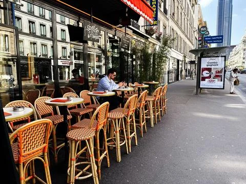 Man using phone at a sunny Paris, France sidewalk cafe terrace with woven w.. 写真素材