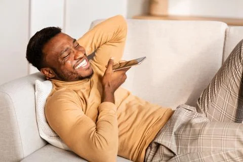 Man Using Phone Voice Assistant Lying On Couch At Home Stock Photos