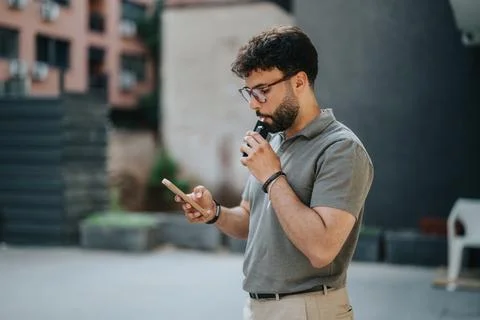 Man using phone while vaping outside in a modern urban environment Stock Photos