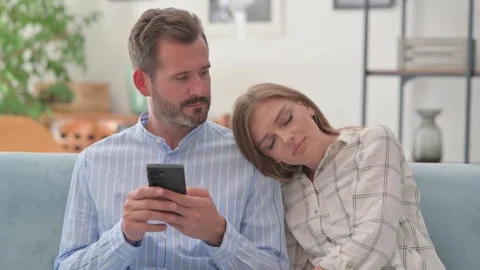 Man Using Phone while Wife Sleeping on Shoulder in Sofa Stock-Footage 287894789