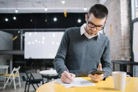 Man using phone while writing on paper sheets Stock Photos