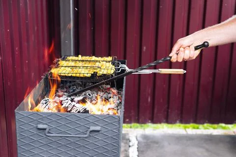 A man using a poker straightens the coals in the grill Stock Photos