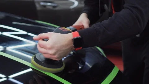 A man using a polishing machine puts varnish on the body of a black car Stock Footage 115934875