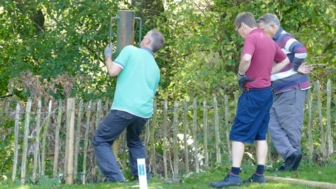 Man using a post rammer, with two other workmen watching. Video stock 119589224