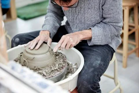 A man using a pottery wheel, shaping a pot base with a small handheld tool Stock Photos