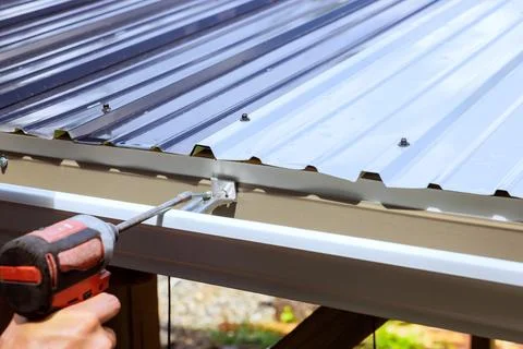 Man using power drill on metal roof during construction in location Stock Photos