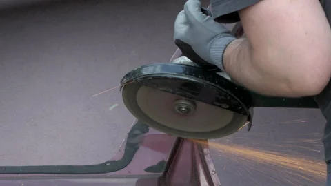 A man using a power tool - an angle grinder to cut a piece of metal car body Stock Footage 226953072