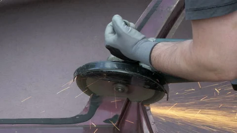 A man using a power tool - an angle grinder to cut a piece of metal car body Stock Footage 226995042