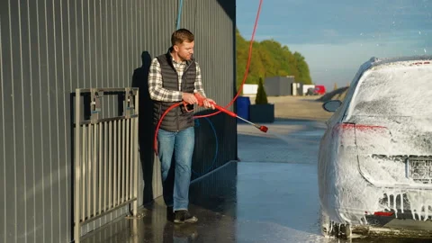 A man using a pressure washer to clean a car covered in soap foam Video stock 297127157