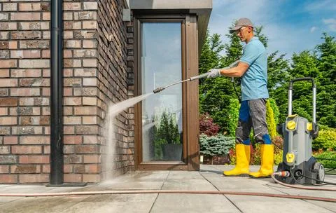 Man Using Pressure Washer to Clean Exterior of Home in Sunny Weather Foto stock