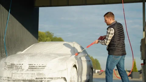 A man using a red pressure washer to apply foam on a car windshield Stock Footage 297127506