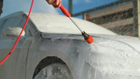A man using a red pressure washer to cover his car in foam at an outdoor self Video stock 297127608