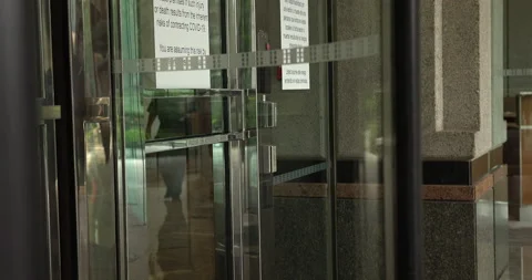 Man Using Revolving Door That Has COVID-19 Warning Bulletin Signage Stock Footage 209592322