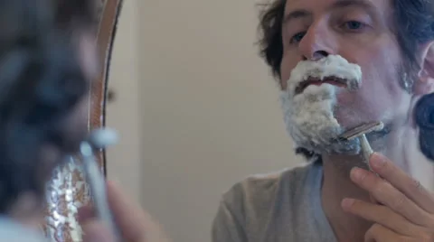 A man using a safety razor to shave in a mirror - dolly shot Stock Footage 67399840