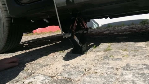 Man using scissor jack to lower vehicle after tire replacement 스톡 동영상 336569447