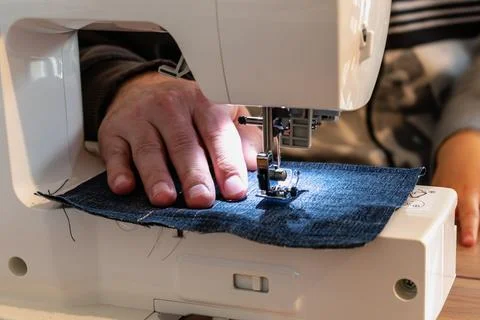 Man using a sewing machine with a blue garment, for repair work, customizat.. 스톡 사진