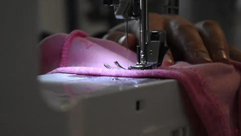 Man using a sewing machine to make a seam on a pink fabric Stock Footage 257788177