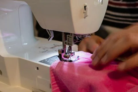 Man using a sewing machine with a pink garment, for repair work, customizat.. 스톡 사진